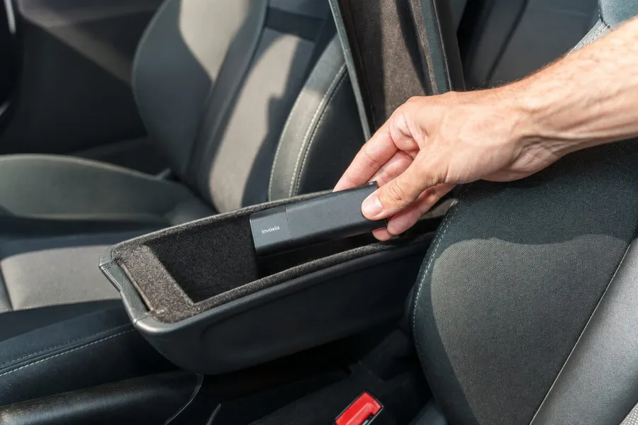 Une main glisse un GPS Tracker Pro Max dans un vide-poches à côté d’un siège de voiture