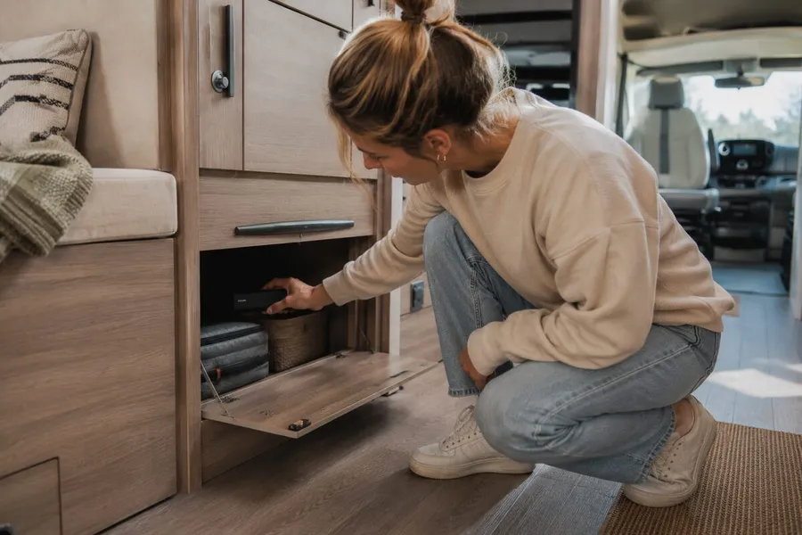 Une femme cache un GPS Tracker Pro Max dans un compartiment de rangement à l’intérieur d’un van aménagé