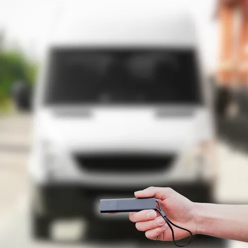 a hand holding a Tracker GPS Pro in front of a utility van