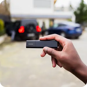 A Classic GPS Tracker held in a hand, with a blurred background showing two cars in a courtyard