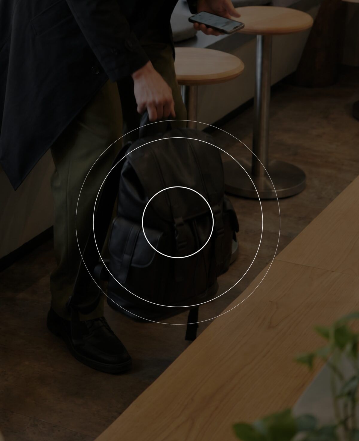 Voyageur prenant un sac à dos dans un café, téléphone à la main, avec des cercles de détection de proximité autour du sac