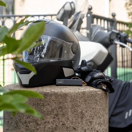 Invoxia GPS tracker placed next to a motorbike helmet, in front of a scooter
