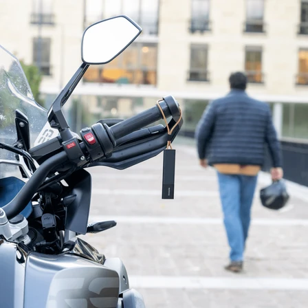 Tracker GPS Invoxia accroché au guidon d'un scooter + homme au loin